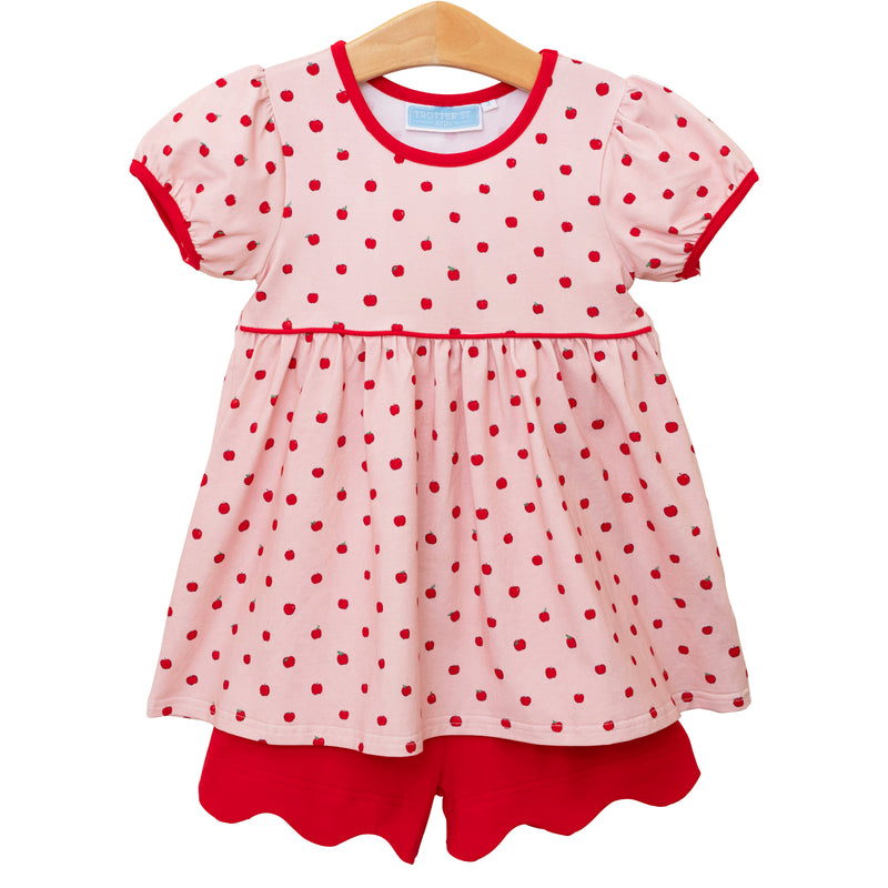 Pink dress with red polka dot apples and trim on a hanger against a white background