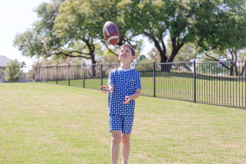 Child in a blue football patterned pajamas playing with a football on a grassy field.