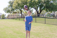 Child in a blue football patterned pajamas playing with a football on a grassy field.