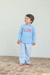Child wearing a blue set with a red fire truck design against a white brick wall.