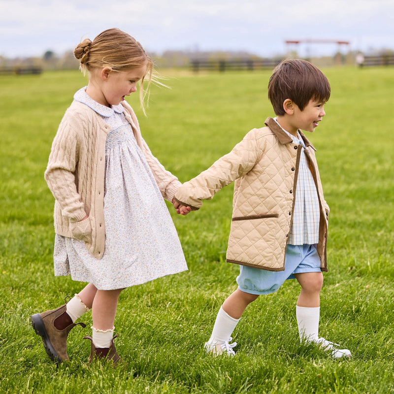 Two children holding hands in a grassy field wearing Little English