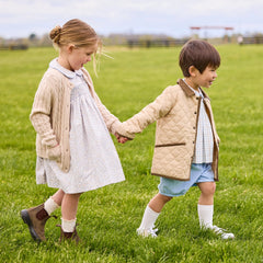 Two children holding hands in a grassy field wearing Little English